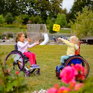 Zwei Kinder sitzen im Kinderrollstuhl und werfen sich einen Spielwürfel zu